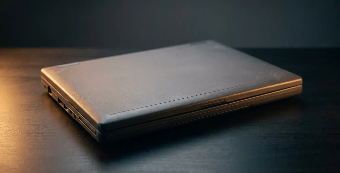 Un ordinateur portable fermé, à l'apparence datée, posé seul sur un bureau sombre