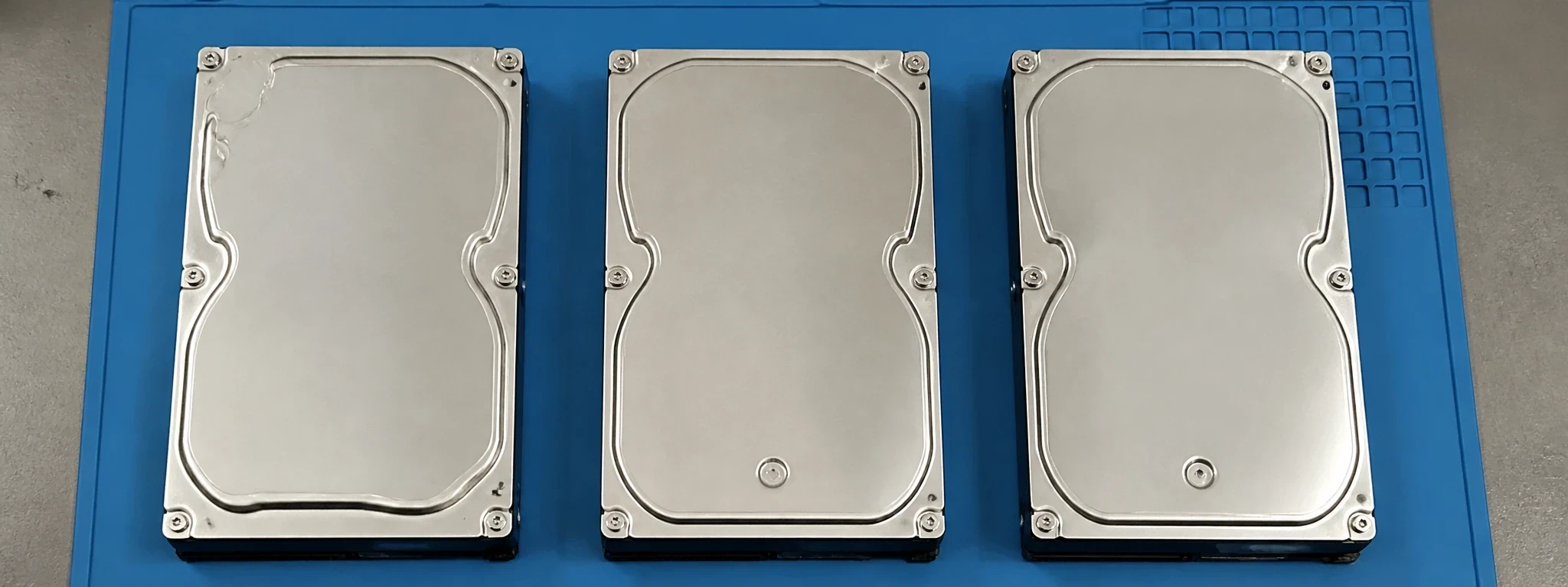 Trois disques durs nus alignés sur un tapis antistatique bleu, vus du dessus