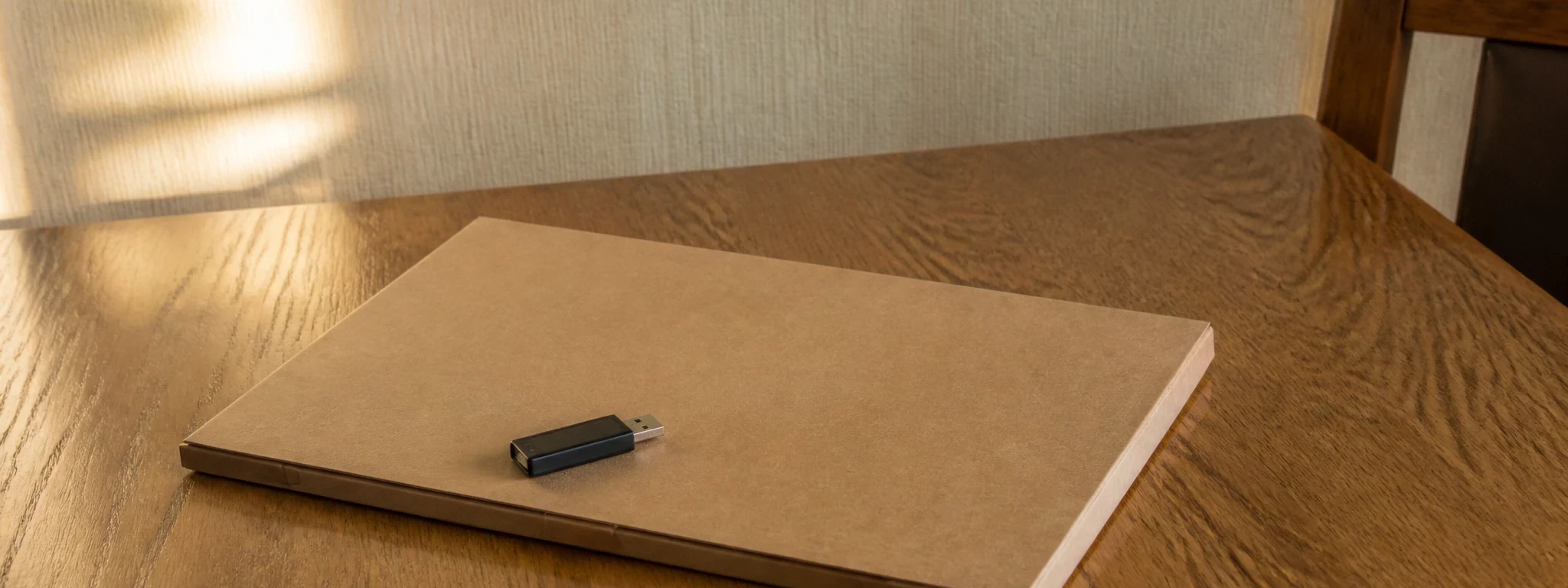 Un dossier cartonné fermé sur une table en chêne, avec une petite clé USB posée dessus