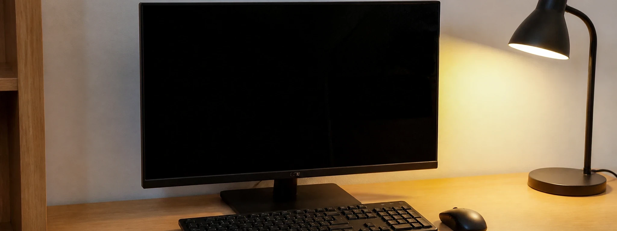 Un bureau en bois clair avec un écran éteint, un clavier et une souris, éclairé par une lampe jaune