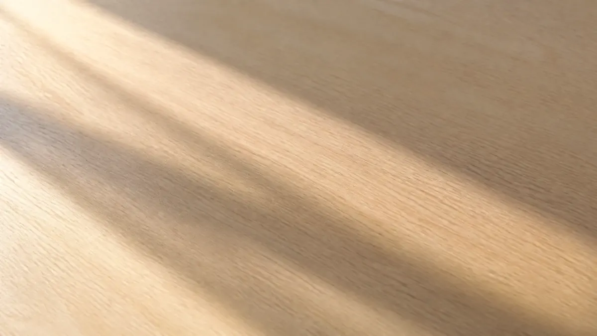 Le grain d'un bureau clair traversé par l'ombre allongée d'un objet hors champ