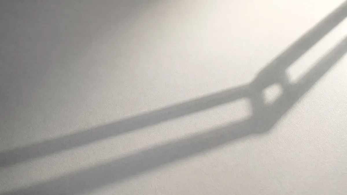 Un plan de travail blanc mat entièrement dégagé, traversé par l'ombre du bras d'une lampe