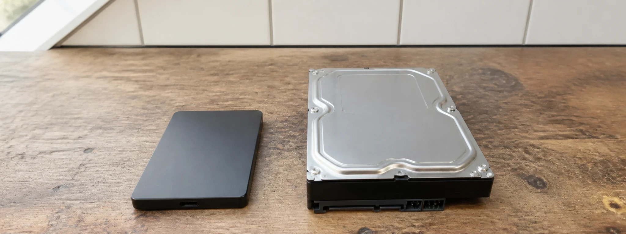 Un petit SSD externe posé à côté d'un disque dur interne de 3,5 pouces, sur un comptoir en bois brut