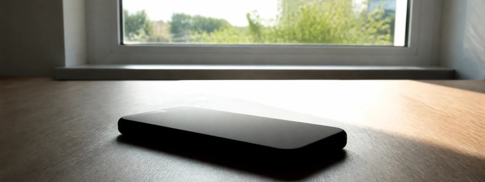 Un téléphone posé face contre un bureau clair, découpé à contre-jour devant une fenêtre