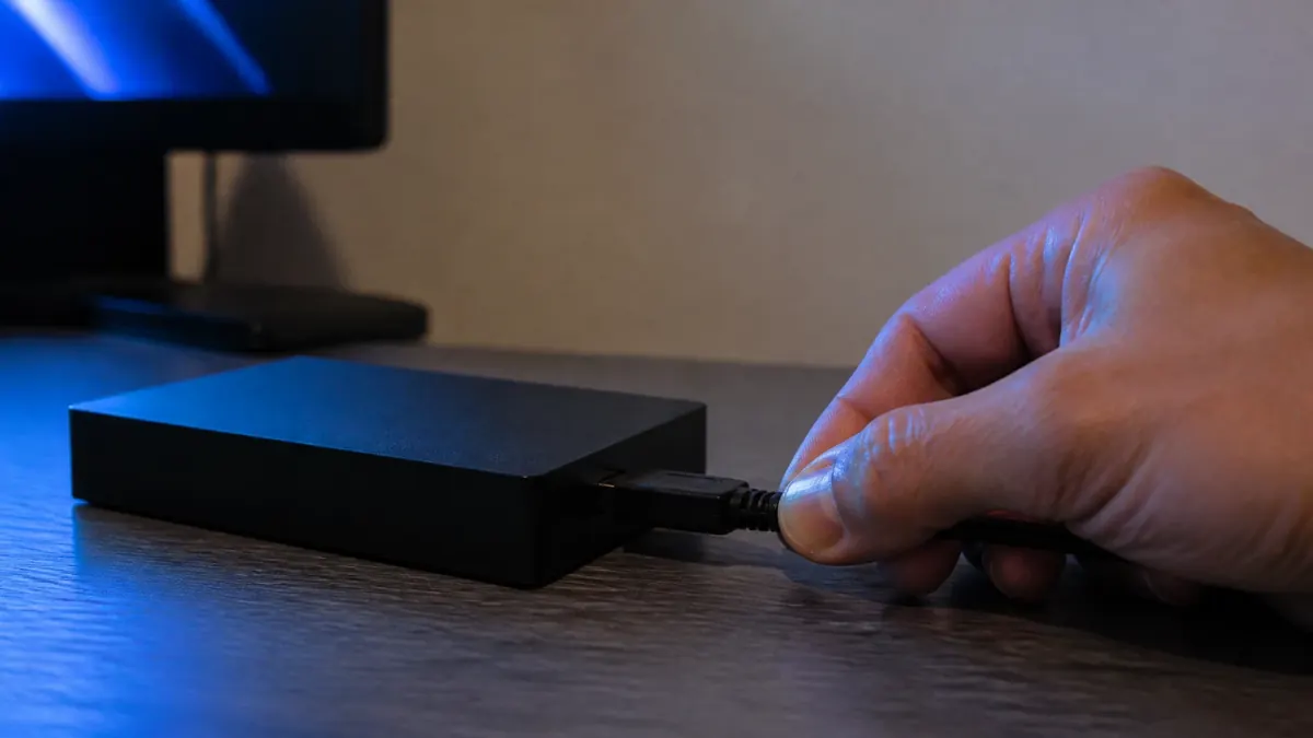 Une main débranche le câble d'un disque externe posé sur le bureau