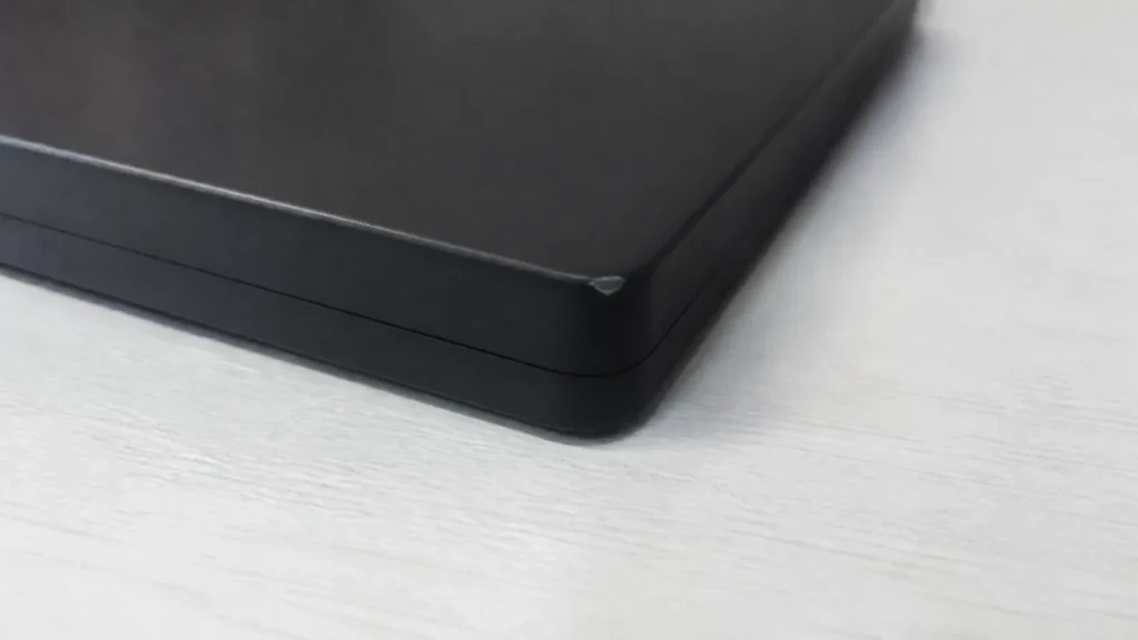 Gros plan sur l'angle éraflé d'un boîtier de disque dur externe noir, posé sur une table blanche